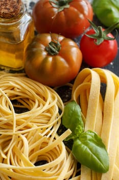 Fresh pasta, olive oil, tomatoes and basil on a dark board