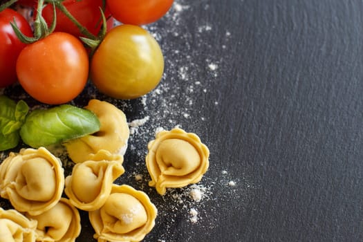 Homemade raw Italian tortellini with fresh tomatoes and basil on a dark background