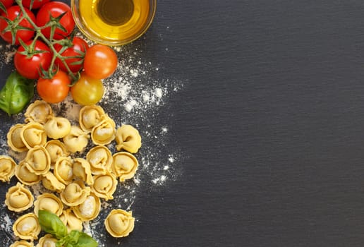 Fresh tortellini pasta and ingredients on a dark board top view