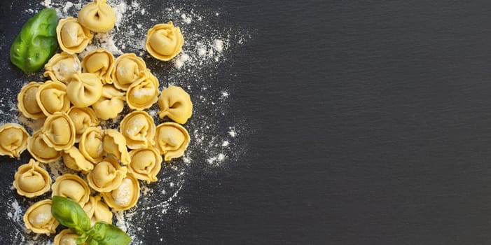 Homemade raw Italian tortellini and basil on a dark background
