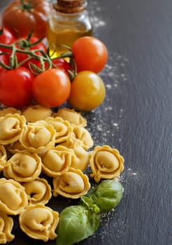 Fresh tortellini and ingredients on a dark board