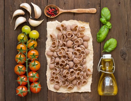 Whole spelt pasta, vegetables, herbs and olive oil on wooden background