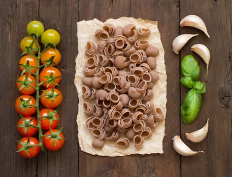 Raw conchiglie pasta, basil and vegetables on wooden background