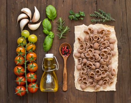 Whole spelt pasta, vegetables, herbs and olive oil on wooden background