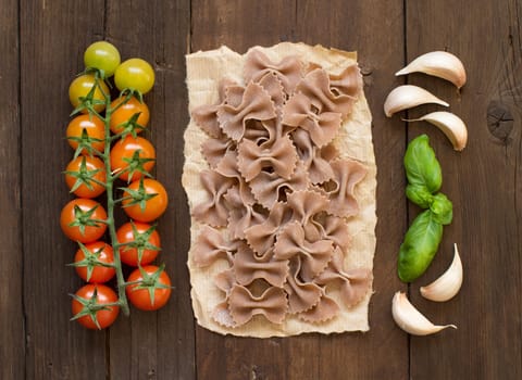 Raw farfalle pasta, basil and vegetables on wooden background
