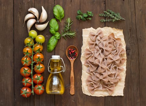 Whole wheat pasta, vegetables, herbs and olive oil on wooden background