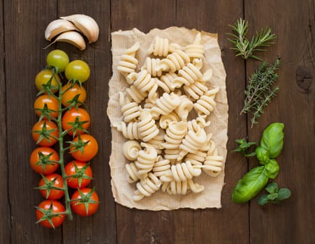 Italian pasta, tomatoes and herbs on wooden background