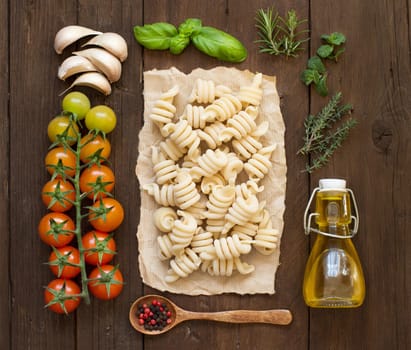 Italian pasta, vegetables, herbs and olive oil on wooden background