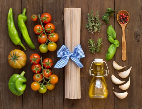 Raw fettucce pasta, vegetables, herbs and olive oil on wooden background
