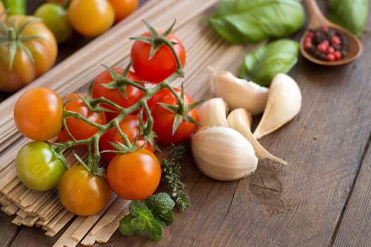 Raw fettuccine pasta, vegetables and herbs on wooden background