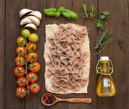 Whole wheat pasta, vegetables, herbs and olive oil on wooden background