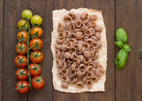 Whole wheat pasta, tomatoes and basil on wooden background