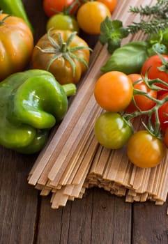 Raw fettucce pasta, vegetables and herbs on wooden background