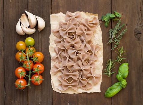 Whole wheat pasta, vegetables and herbs on wooden background