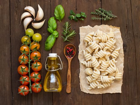 Italian pasta, vegetables, herbs and olive oil on wooden background