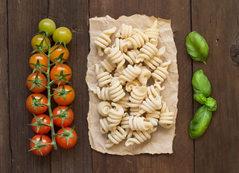Whole wheat pasta, tomatoes and basil on wooden background