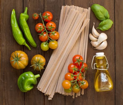 Raw fettucce pasta, vegetables and olive oil on wooden background