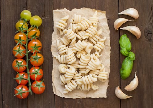 Raw italian pasta, basil and vegetables on wooden background