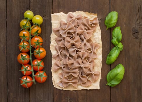 Whole wheat pasta, tomatoes and basil on wooden background