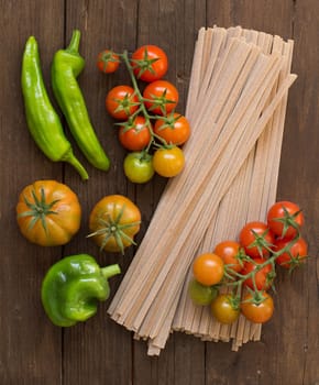 Raw fettuccine pasta and vegetables on wooden background