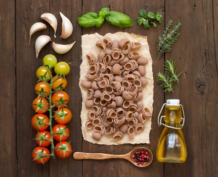 Whole spelt pasta, vegetables, herbs and olive oil on wooden background