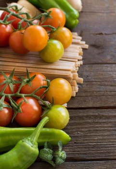 Raw fettucce pasta, vegetables and herbs on wooden background