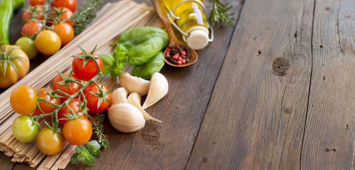 Raw fettucce pasta, vegetables, herbs and olive oil on wooden background
