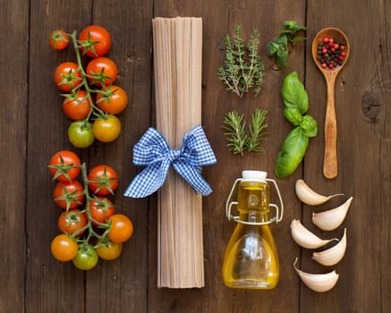 Raw fettuccine pasta, vegetables, herbs and olive oil on wooden background