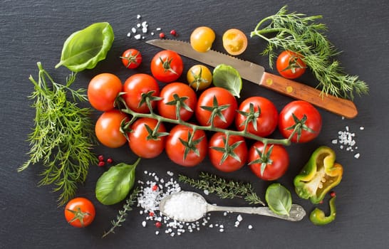 Cherry tomatoes, herbs and salt on a dark board