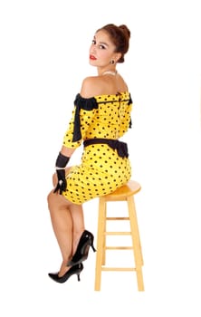 A beautiful young woman sitting from the back on a chair in a yellow .dress and black cloves, isolated for white background..
