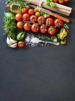 Cherry tomatoes, herbs, pasta and olive oil on a dark board