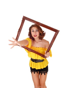 A angry woman in a yellow blouse and black shorts stretching her hand.trough a picture frame, isolated for white background..