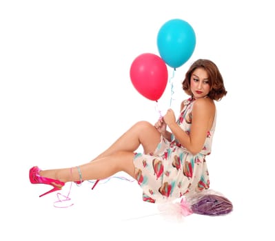 A beautiful young woman sitting on the floor holding two balloons and.a lollypop, isolated for white background..