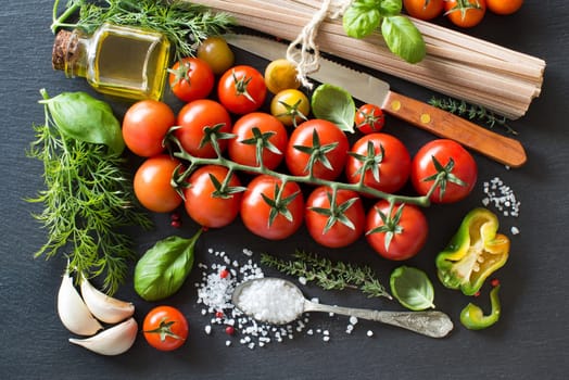 Italian cooking ingridients : cherry tomatoes, herbs, pasta and olive oil on a dark background