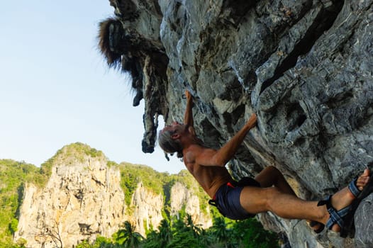 a strong and happy man climbing on high rock over the sea with a hut and a. Tonsai beach in Thailand