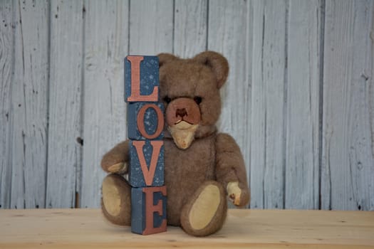 Old antique teddy bear with stacked letter cubes,with the word love in front of old white wooden wall