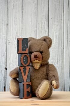 Old antique teddy bear with stacked letter cubes,with the word love in front of old white wooden wall