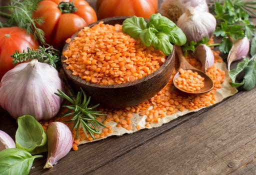 Red lentils in a bowl with tomatoes, garlic and herbs on wood