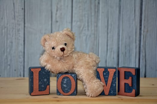Little white teddy bear lies on cubes with the word Love in front of a white wooden wall