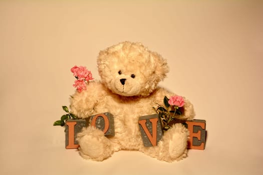 White Teddy Bear sits with Love Bau stones against a light background and pink roses
