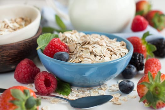 Rolled oats in a bowl with berries and milk on wood