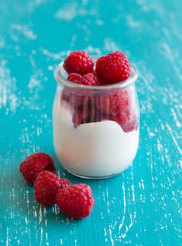 Raspberries and fresh yogurt in a jar on a turquoise background