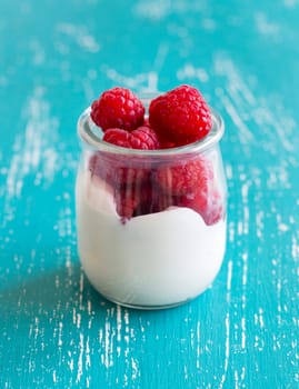 Raspberries and fresh yogurt in a jar on a turquoise background