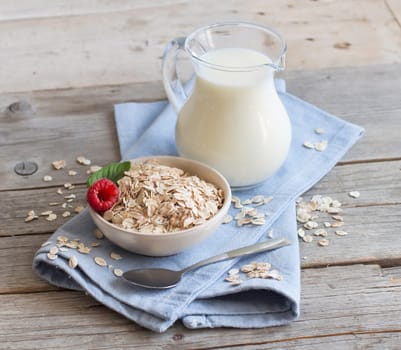 Rolled oats in a bowl with berries and milk on wood
