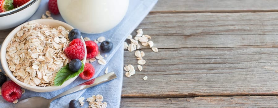 Rolled oats in a bowl with berries and milk on wood