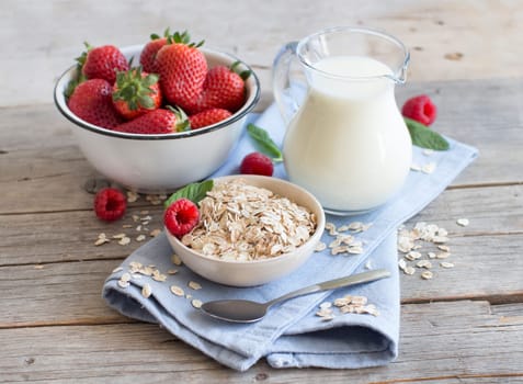 Rolled oats in a bowl with berries and milk on wood