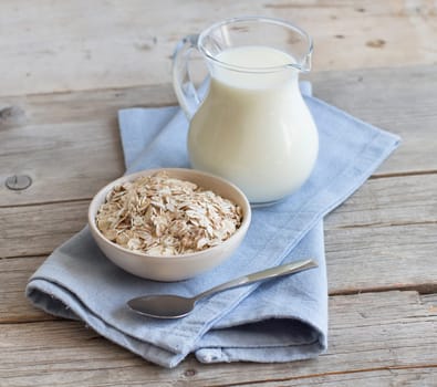 Rolled oats in a bowl and milk on a wooden table