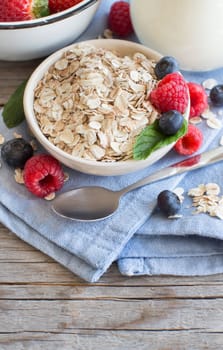 Rolled oats in a bowl with berries and milk on the wooden table