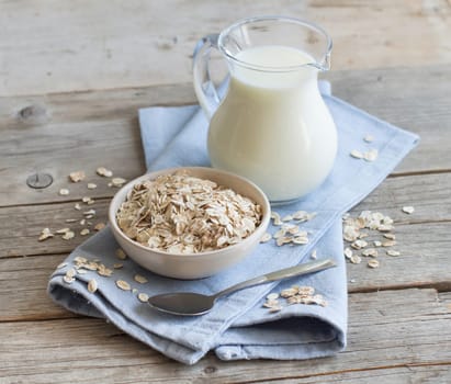 Rolled oats in a bowl and milk on a wooden table