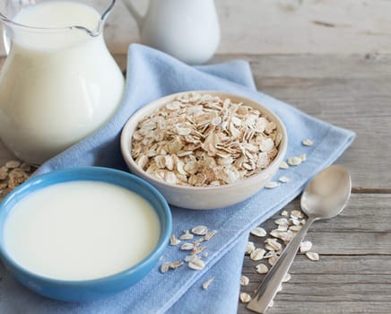 Rolled oats in a bowl and milk on a wooden table